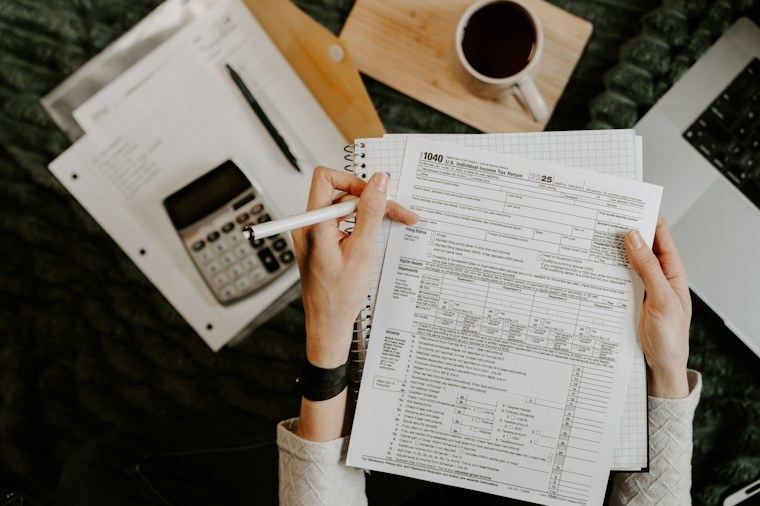 Mãos conferindo documentos financeiros com calculadora e notebook sobre a mesa