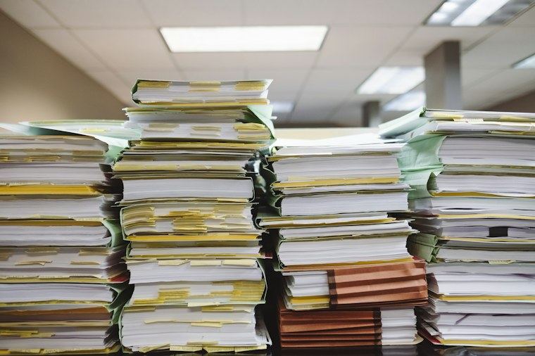 Pilhas de pastas e documentos empilhados sobre uma mesa de escritório