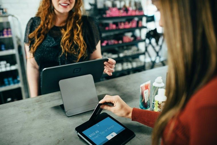 Cliente pagando na maquineta enquanto a atendente usa o sistema no tablet